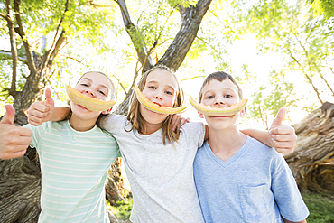 Caucasian boy and girls smiling with cantaloupe rinds