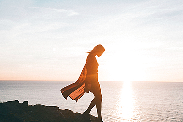 Silhouette of Caucasian woman walking on rocks at ocean