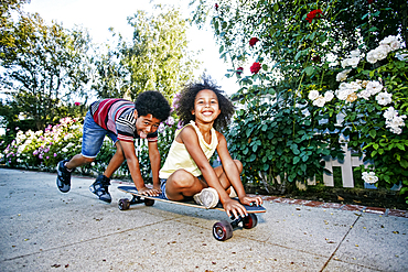 Mixed Race boy pushing sister on skateboard on sidewalk