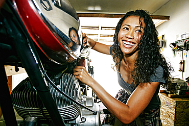 Laughing Mixed Race woman repairing motorcycle in garage