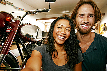 Man and woman posing for selfie with motorcycle in garage