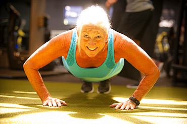 Smiling older woman doing push-up on gymnasium floor