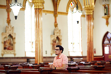 Kneeling Hispanic man praying in church pew