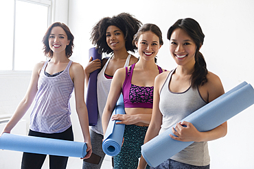 Smiling women holding rolled up exercise mats