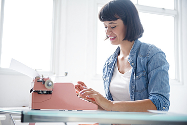 Hispanic woman typing on pink typewriter