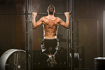 Caucasian man doing chin-up in gymnasium