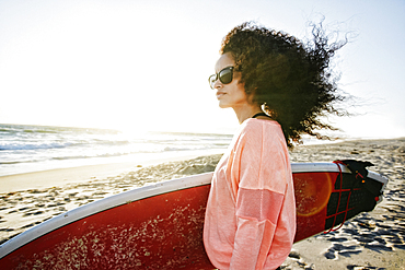 Hispanic woman holding surfboard at beach