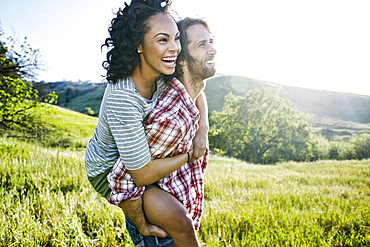 Smiling Man carrying girlfriend piggyback on hill