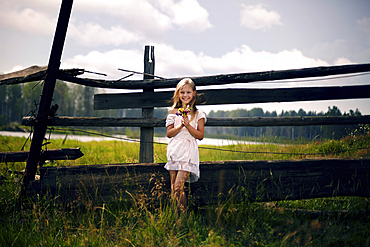 Caucasian girl holding bouquet of wildflowers leaning on wooden fence