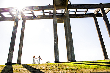 Caucasian brides holding hands walking under concrete structure