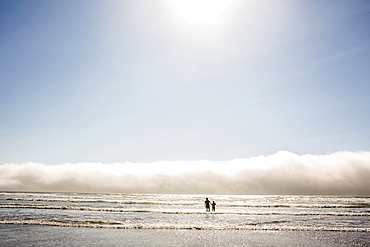 Caucasian mother and son wading in ocean waves at beach