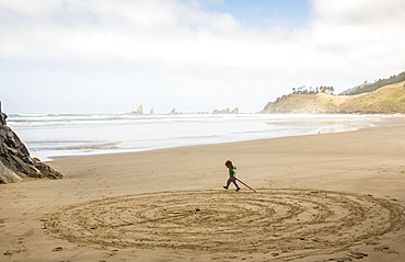 Caucasian girl drawing circles on beach with stick