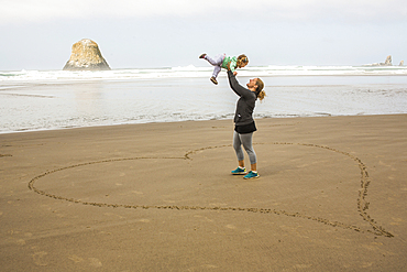 Caucasian mother lifting daughter in heart-shape on beach