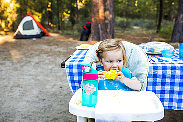 Caucasian girl eating corn in high chair