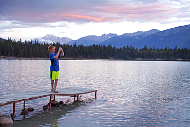 Caucasian boy standing on wooden dock photographing lake