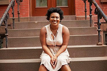 Portrait of smiling Black woman sitting on urban front stoop