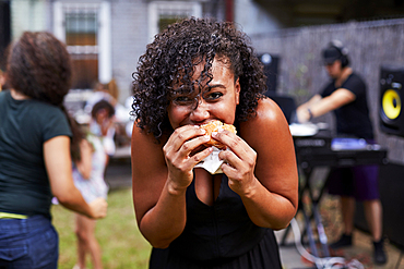 Mixed Race woman eating hamburger at backyard party