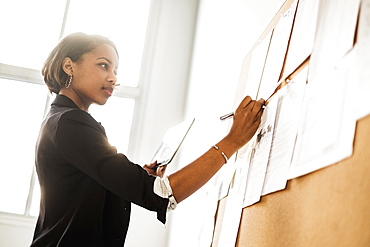 Black businesswoman using digital tablet writing on paperwork