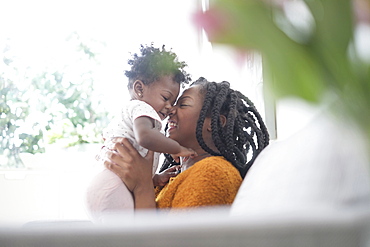 Black woman rubbing noses with baby daughter on sofa