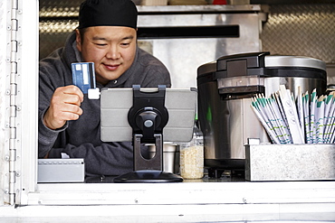 Asian man processing credit card using digital tablet at food cart