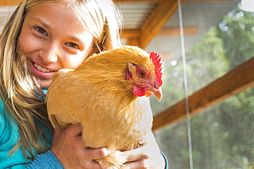 Caucasian girl hugging chicken in chicken coop