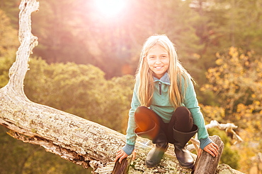 Caucasian girl crouching on log