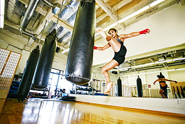 Asian woman kicking heavy bag in gymnasium