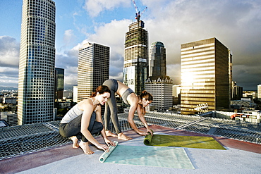 Caucasian women rolling exercise mats on urban rooftop after yoga