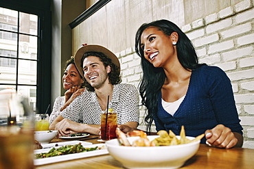 Smiling friends enjoying food and cocktails at table in bar