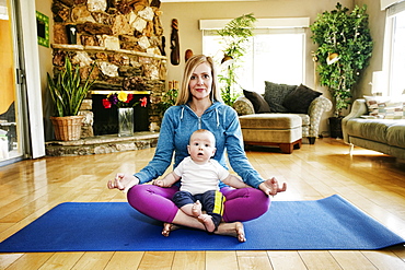 Mother meditating on exercise mat with baby in lap