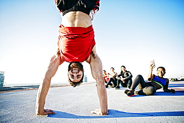 Woman photographing man doing handstand on urban rooftop