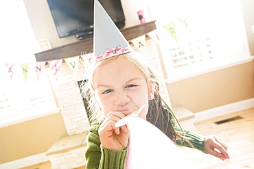 Caucasian girl wearing party hat blowing party horn blower