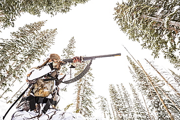 Caucasian woman hunting in forest aiming rifle