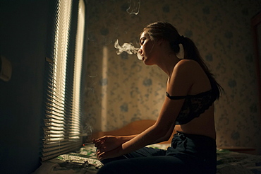 Caucasian woman smoking in bedroom