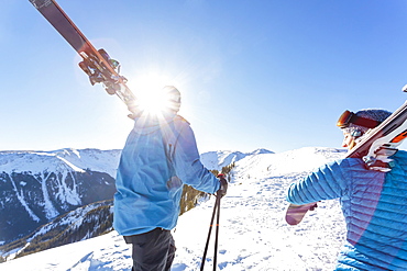 Couple carrying skis on snowy mountain