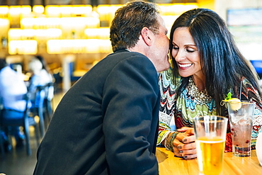 Caucasian man whispering to ear of woman in restaurant