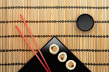 Chopsticks and sushi on square plate with dipping sauce