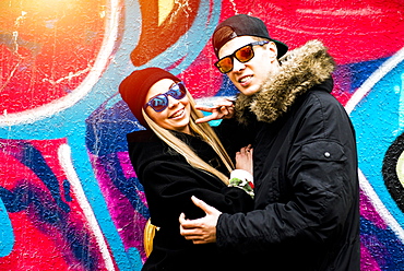 Couple gesturing peace at graffiti wall