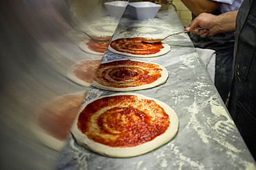 Man putting tomato sauce onto fresh hand made pizzas