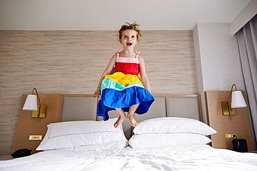 Smiling girl (4-5) jumping on bed