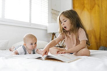 Girl (2-3) reading book to baby brother (6-11 months)