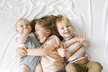 Siblings (6-11 months, 2-3) hugging on bed