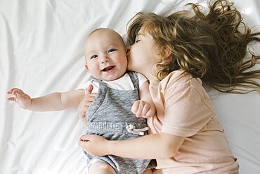 Girl (2-3) kissing and hugging baby brother (6-11 months)