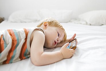 Boy (2-3) using phone in bed