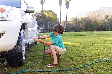 South Africa, Stanford, Boy (8-9) washing wheel of SUV on green lawn