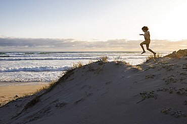 South Africa, Hermanus, Boy (8-9) jumping on sand dune