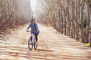 Teenage girl (16-17) riding bicycle on tree lined road