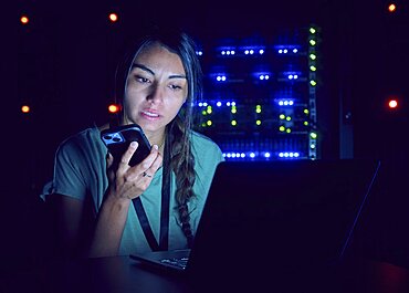 Female technician using laptop and smart phone in server room