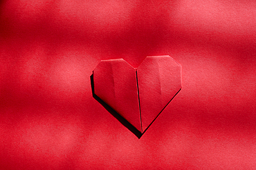 Red origami heart on red background 