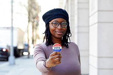 Portrait of smiling woman showing Vote button in city